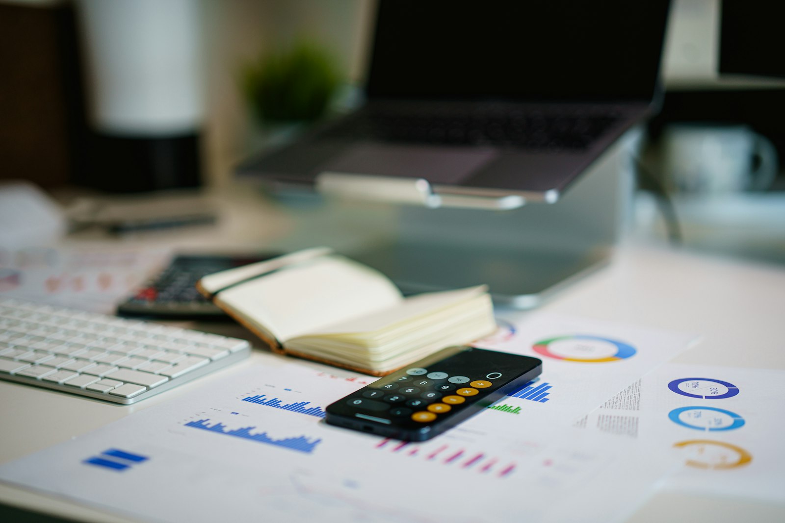 A desk with a smartphone calculator resting on printed financial bar charts, near a keyboard and notebook.