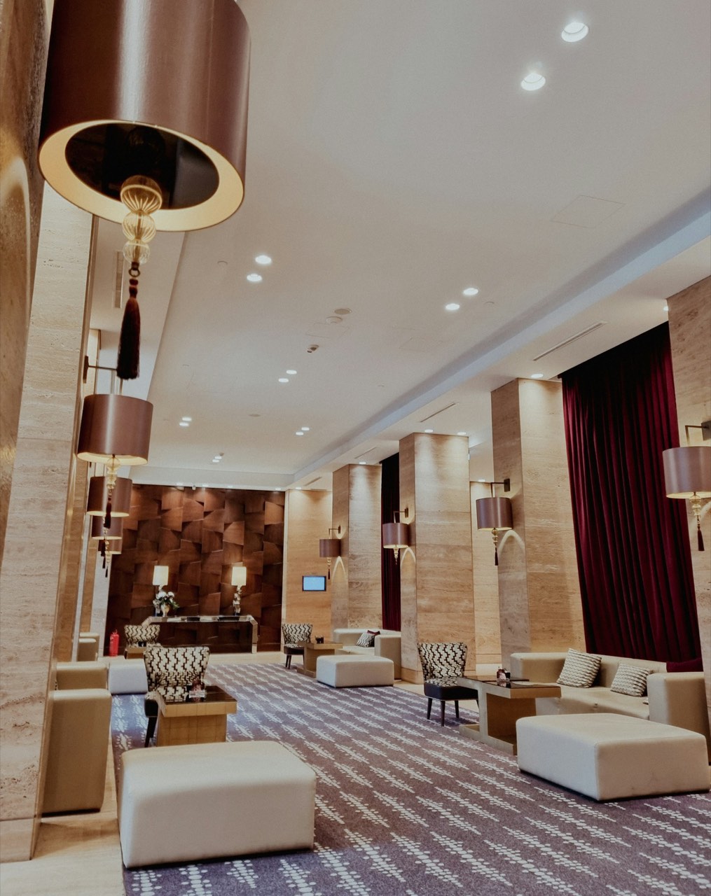 A softly lit hotel lobby corridor with lounge seating and hanging pendant lamps.