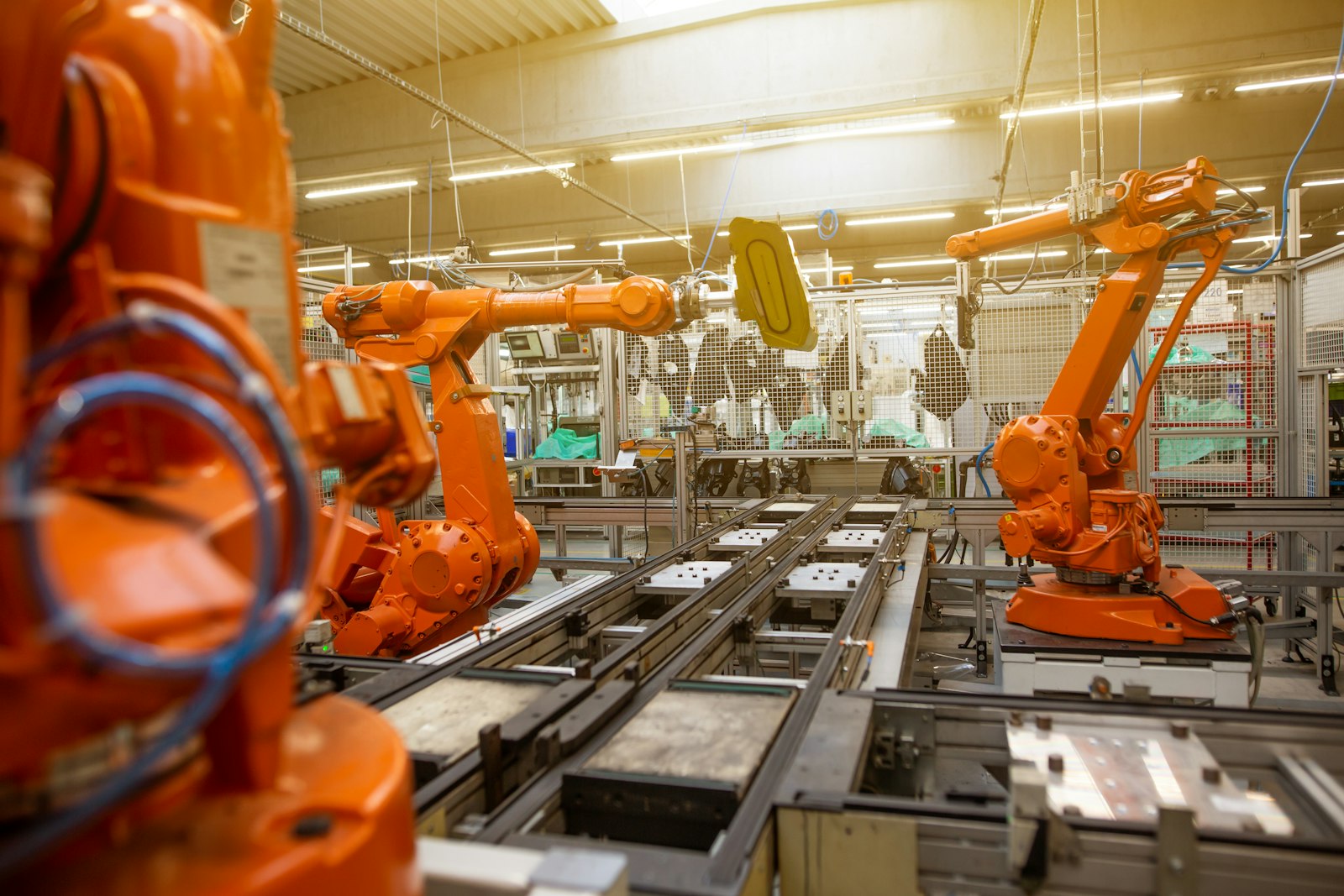 Orange industrial robotic arms positioned along an automotive assembly line inside a bright factory.