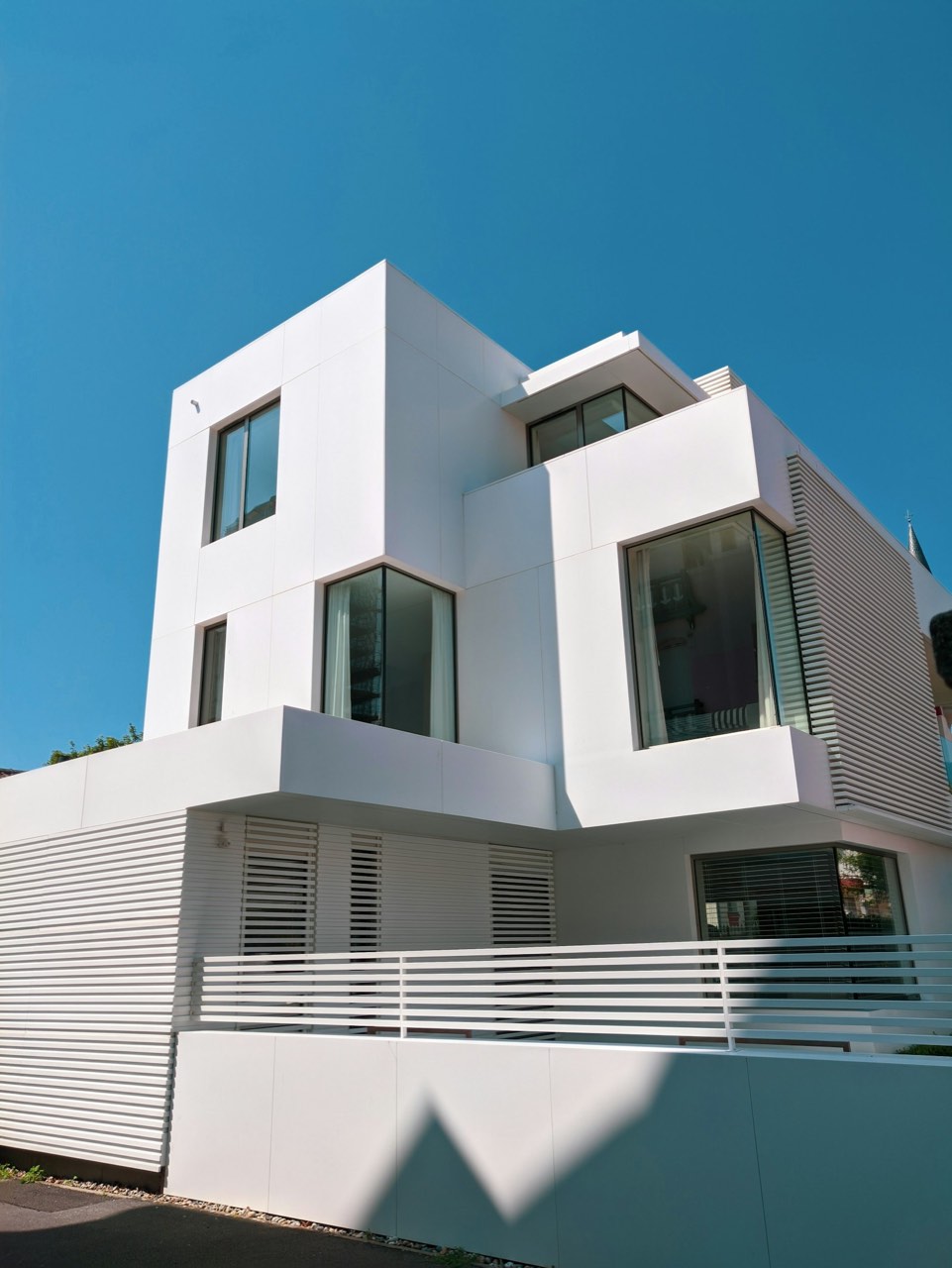 A white modern multi-story house with large windows under a clear blue sky.