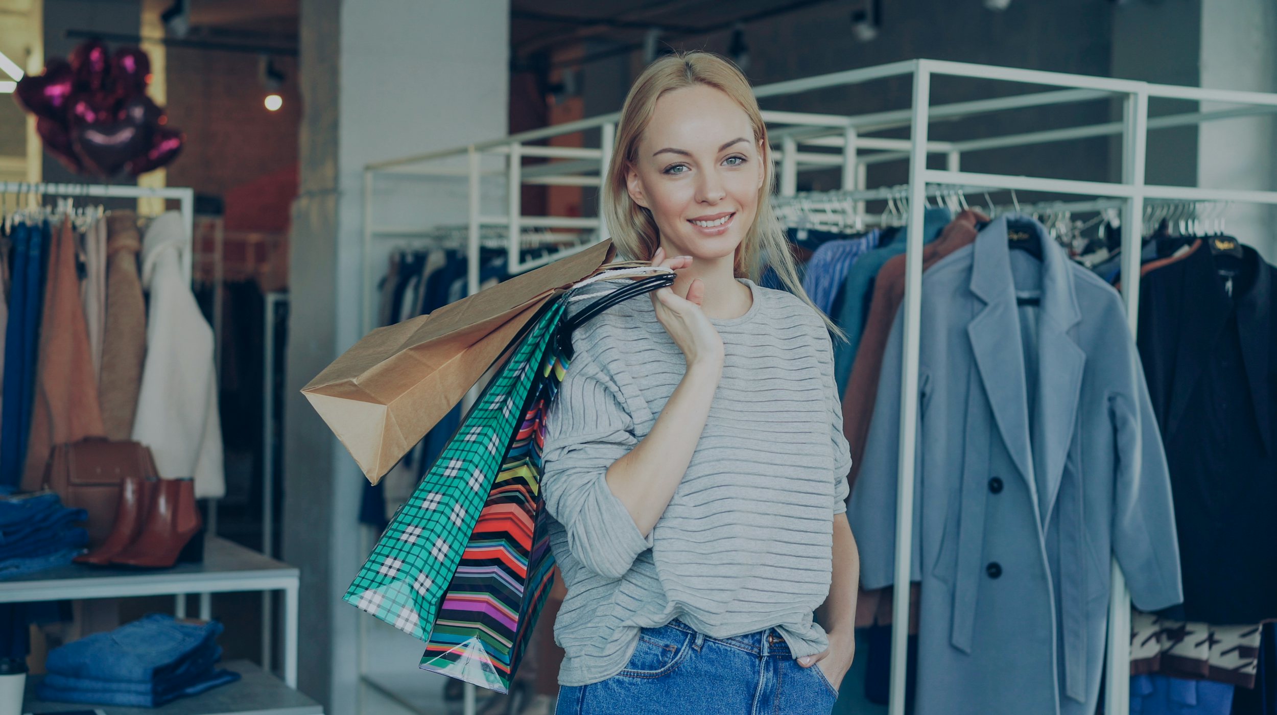 A smiling woman carrying an armful of colorful shopping bags in a clothing store.