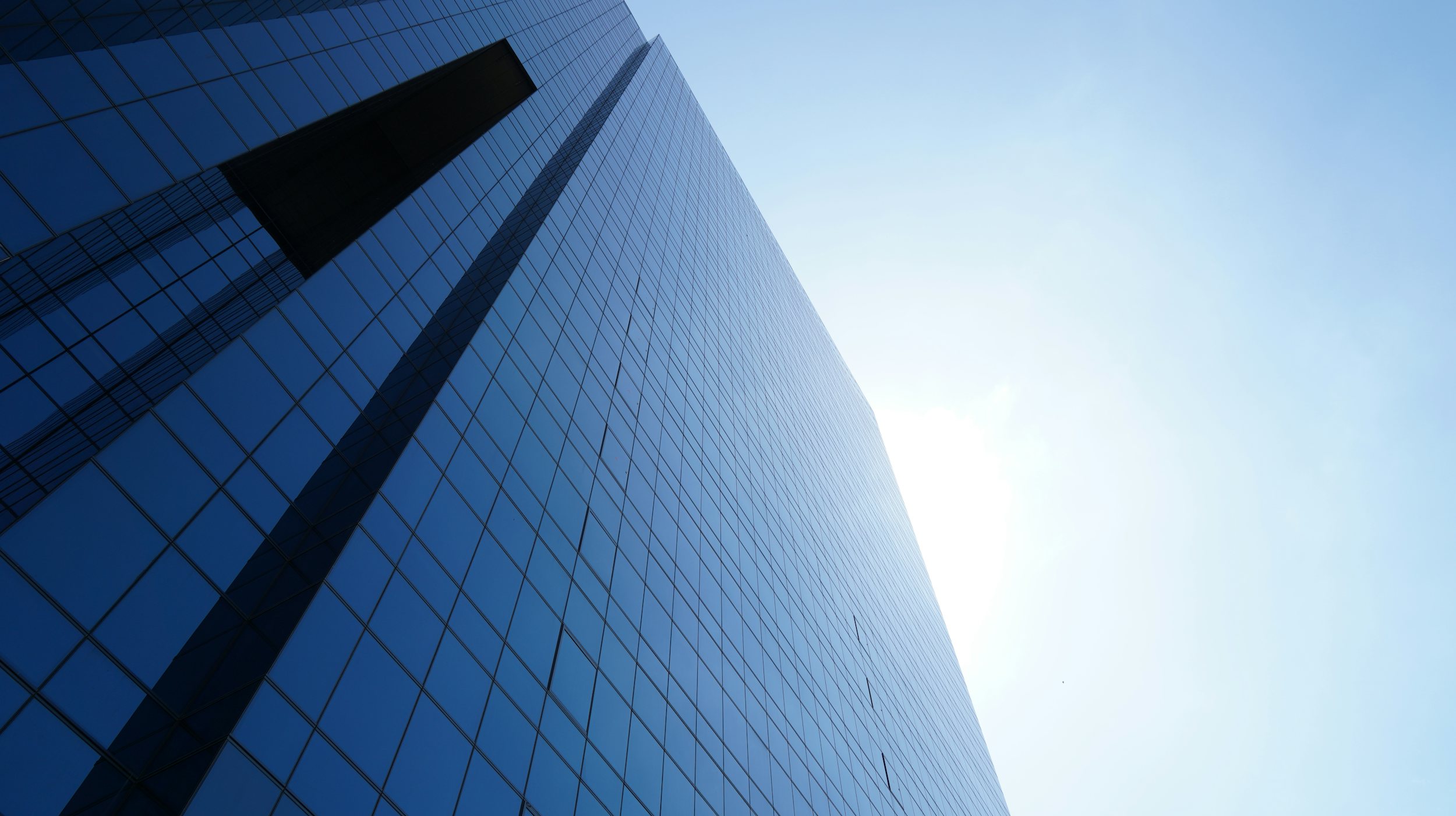 A low-angle view of a modern glass office tower against a clear blue sky.