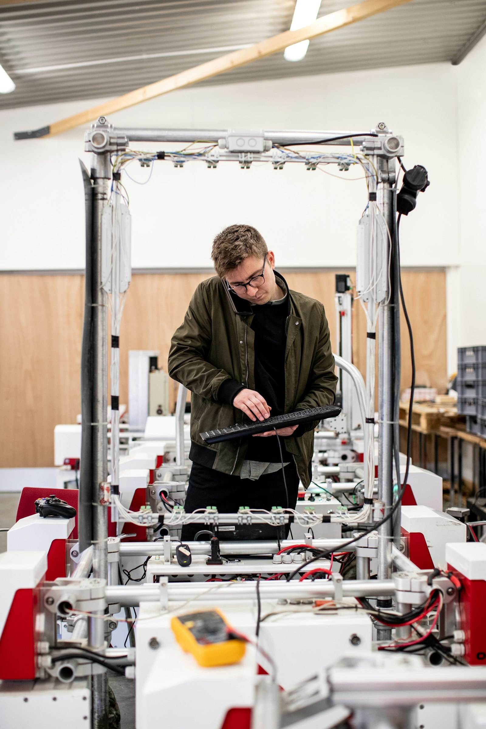 An engineer holding a keyboard while working on a wired testing rig in a workshop.