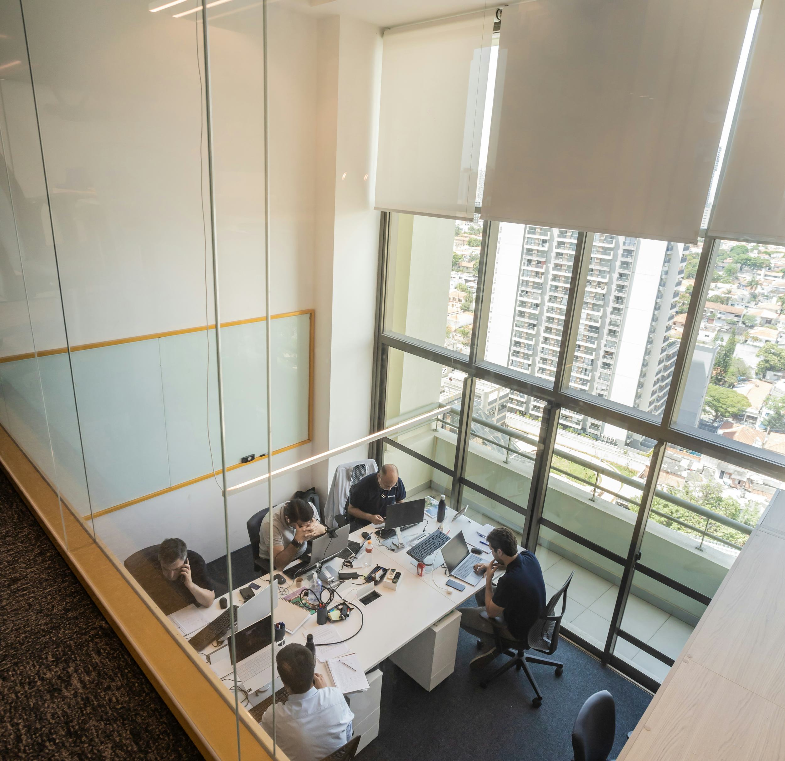 People working at desks in a glass-walled office with a city view in the background.